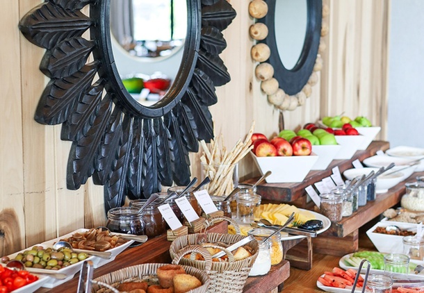 Rustic breakfast buffet with sliced breads, wicker baskets, jams, bowls of fresh fruit and decorative round wooden mirrors.