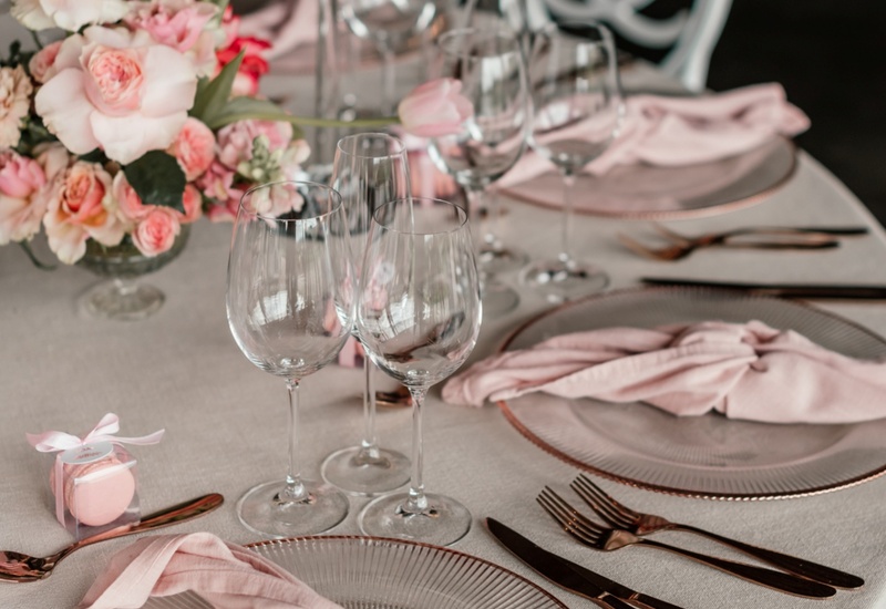 Elegant reception table with blush napkins, glass chargers, rose-gold cutlery, wine glasses and pink floral centerpiece