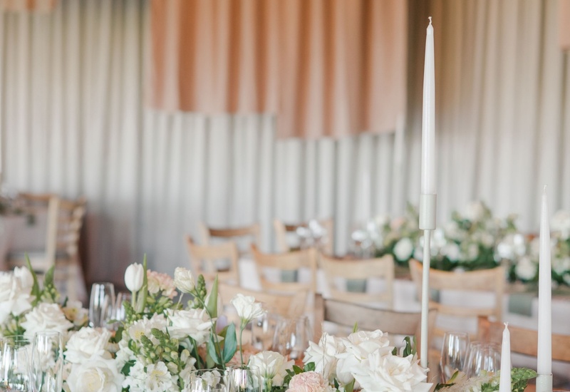 Elegant reception table with white roses, greenery garland, glassware, tall taper candles and soft pendant lighting