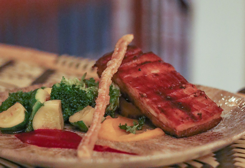 Glazed grilled salmon fillet with roasted zucchini and broccoli, vibrant purees and a crispy thin garnish on a ceramic plate