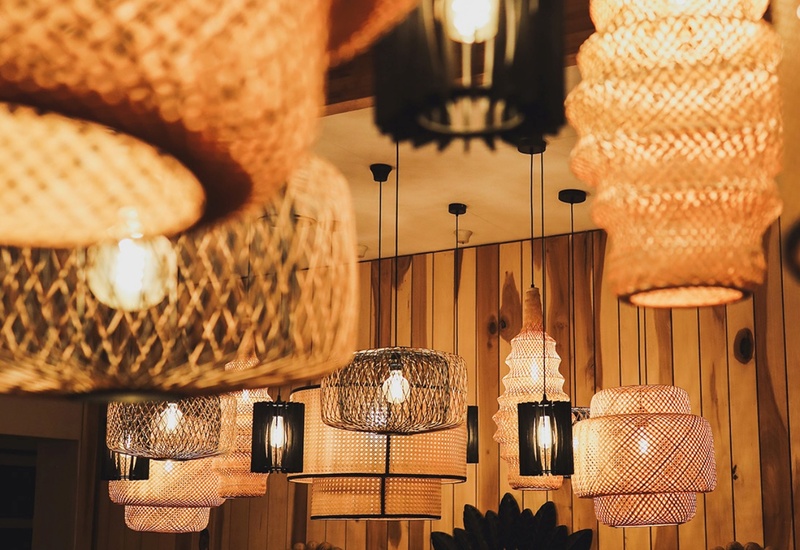 Warm woven pendant lights in a wood-paneled dining area, soft ambient glow over table with decorative mirrors and plants