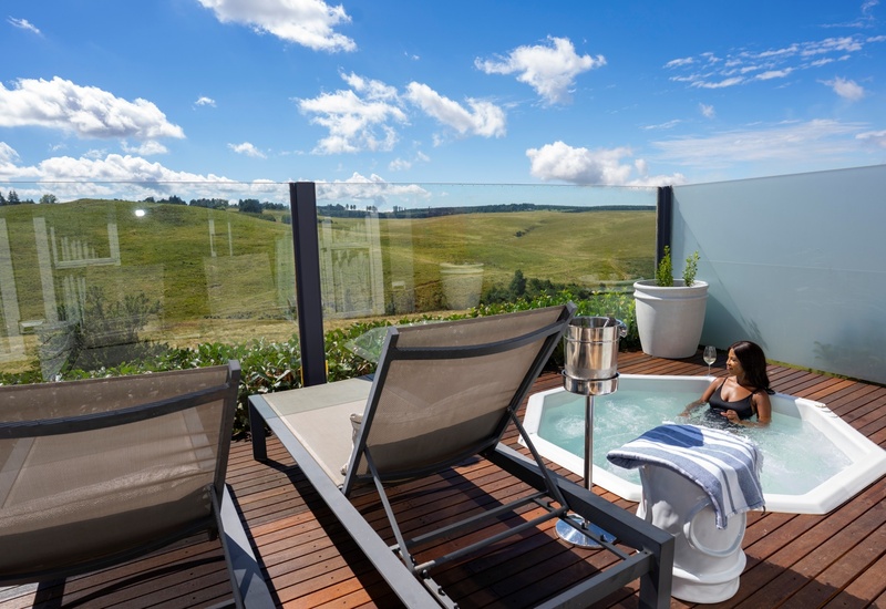 Private rooftop terrace with hot tub, guest relaxing with wine, chilled champagne, loungers and panoramic green hill views.