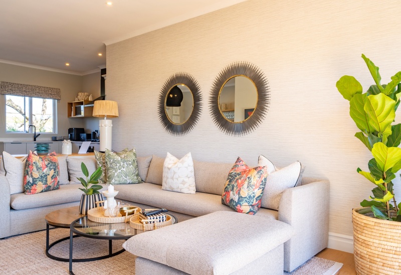 Bright modern suite lounge with sectional sofa, patterned cushions, sunburst mirrors, coffee tables and fiddle-leaf fig.