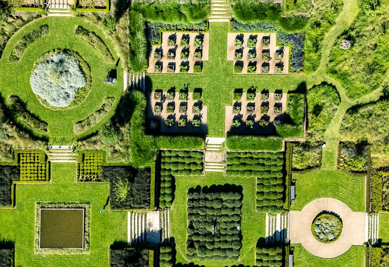 Aerial view of manicured hotel gardens with symmetrical hedges, circular lawn, raised planting beds and sunlit pathways