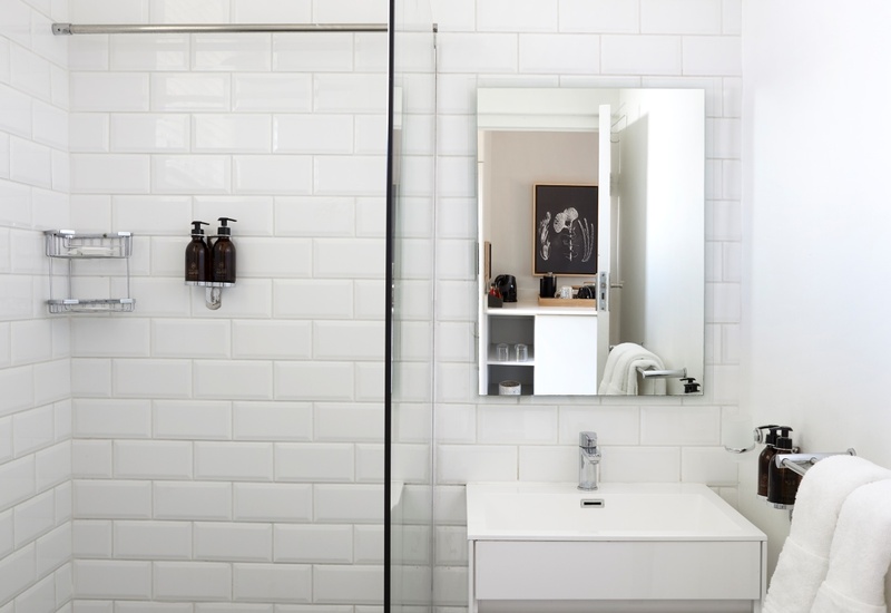 Modern en-suite bathroom with rainfall shower, glass partition, white subway tiles, patterned black-and-white floor, floating vanity and plush towels.