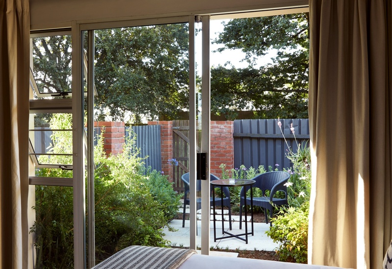 Guest room with sliding glass door and curtains opening onto a private garden patio with round table and two chairs.