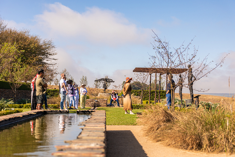 Landscaped hotel terrace with long reflecting pool, pergola seating and guests strolling with countryside views