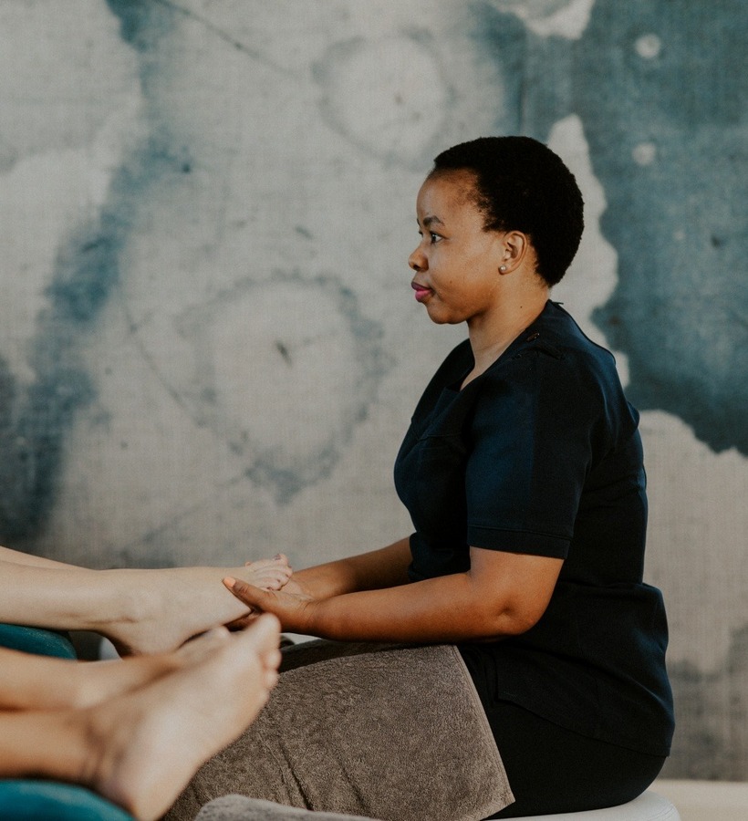 Spa therapist giving a relaxing foot massage to guests reclining in white robes, champagne nearby, serene lounge.
