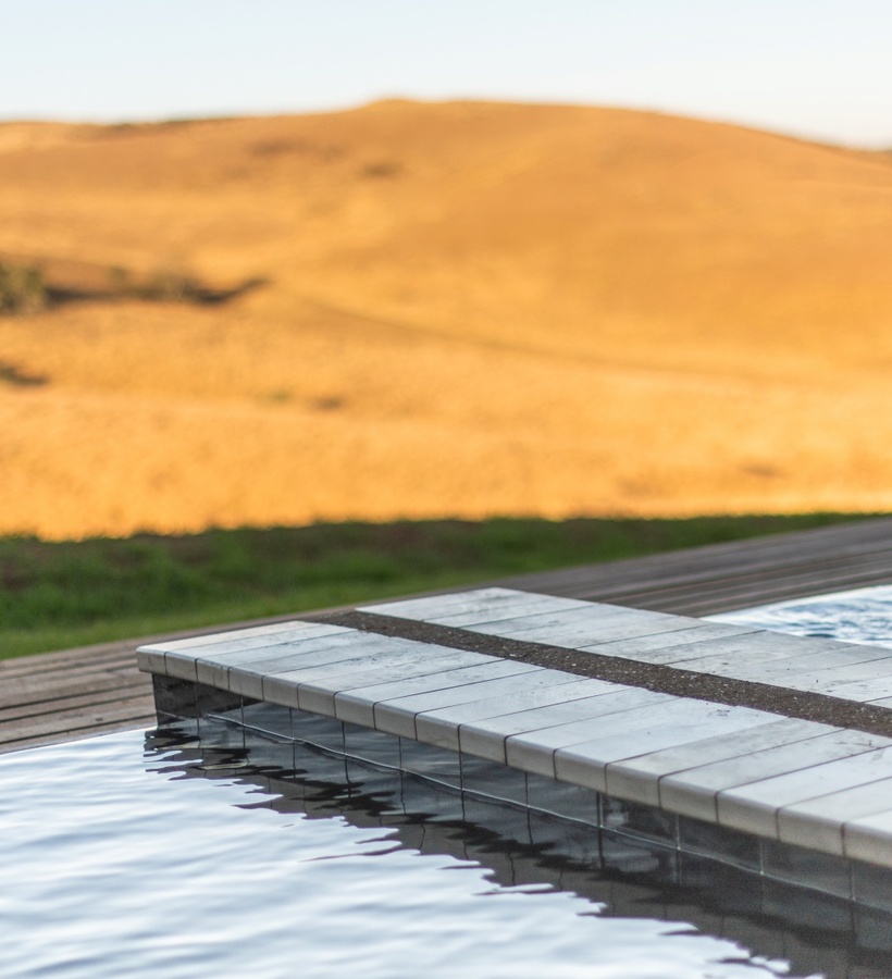 Infinity pool edge and wooden deck overlooking sunlit golden rolling hills, a peaceful countryside terrace for relaxation