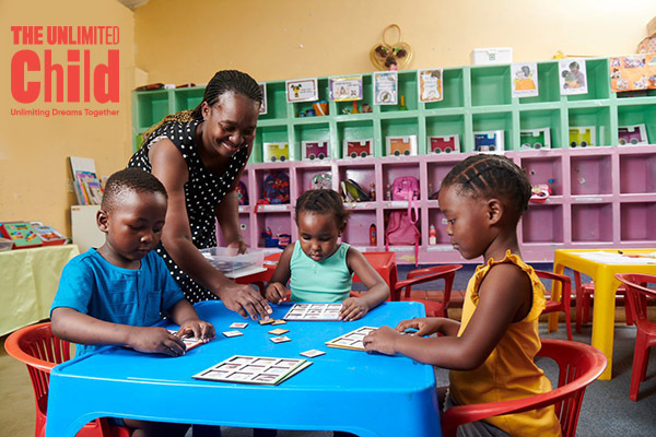 Hotel kids' club: caregiver helping three children at a bright blue activity table with puzzles and colorful cubbies