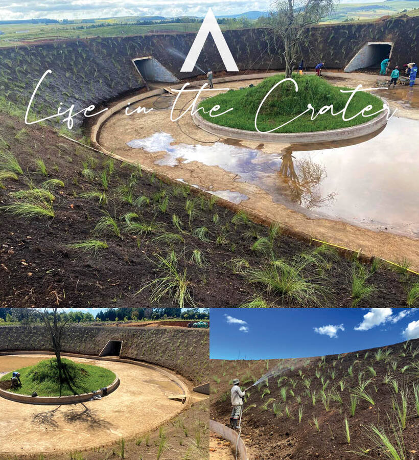Crater-like circular reflecting pool with central grassy island and tree, terraced planted slopes and workers landscaping.