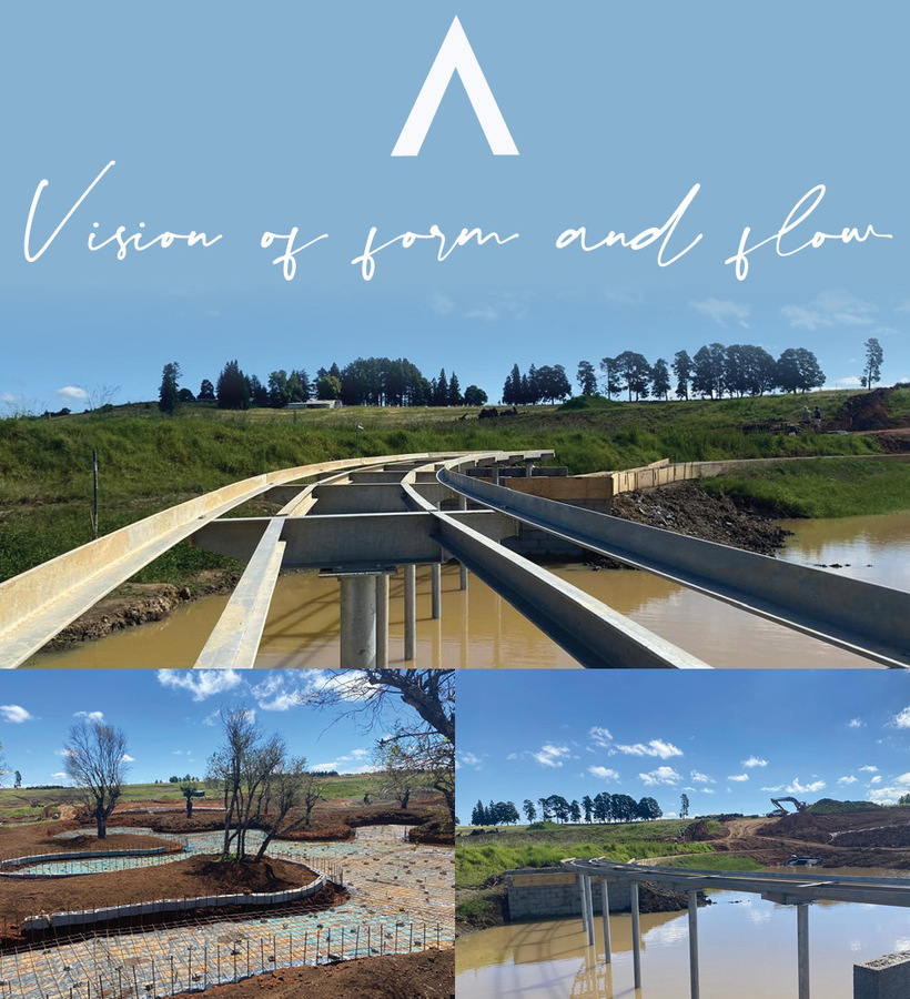 Curved elevated walkway under construction over ponds, landscaped terraces and rolling green hills under blue sky.