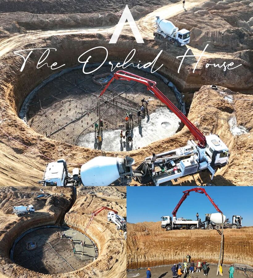 Circular pool foundation under construction, concrete pump and mixer trucks pouring slab while workers smooth rebar-lined base.