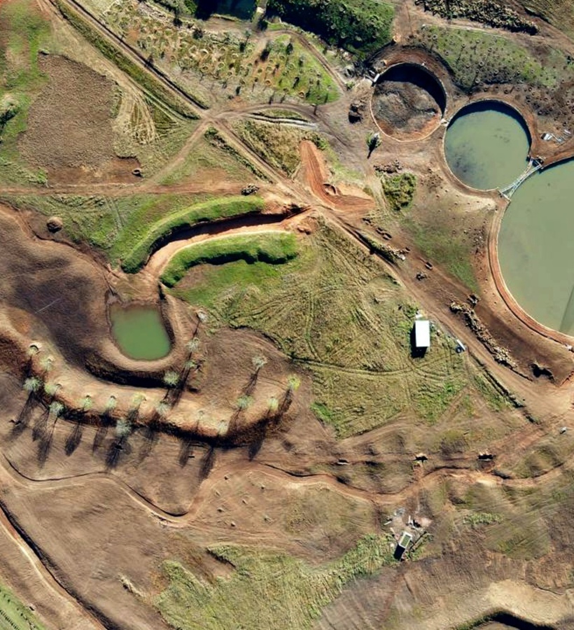 Aerial view of sculpted parkland with circular ponds, earth terraces, winding walking trails and a central fountained lagoon.