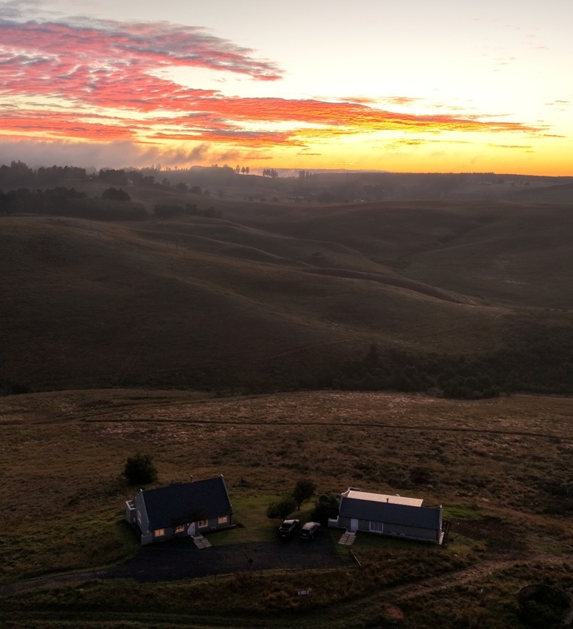 Two cozy countryside cottages with lit windows overlooking rolling hills at sunrise, panoramic rural retreat.