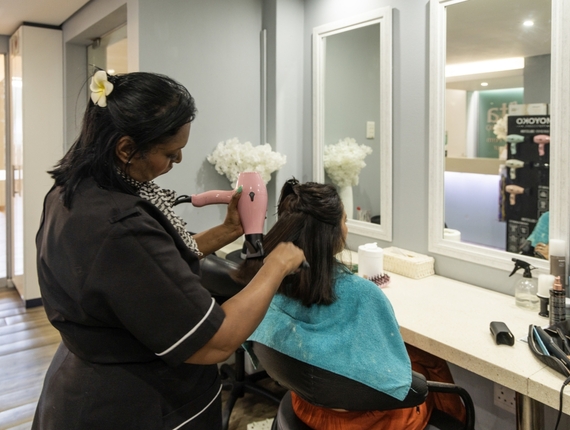 On-site salon stylist blow-drying guest's hair at a vanity mirror, with towels, styling tools and floral decor nearby.
