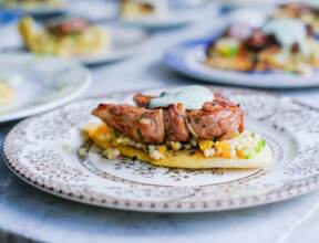 Grilled meat topped with herb sauce served on a bed of pearl couscous and vegetables on a decorative plate