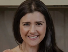 Smiling woman with long dark hair in a warm indoor setting, conveying friendly hospitality and welcoming atmosphere