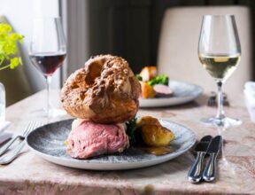 Elegant dining with roasted beef, Yorkshire pudding, side vegetables, paired with glasses of red and white wine on a marble table