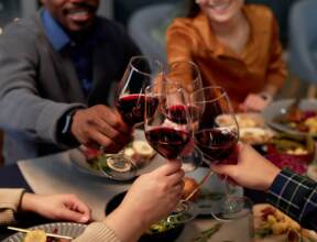 Guests clinking glasses of red wine over a gourmet meal in a cozy dining setting, celebrating together at the table