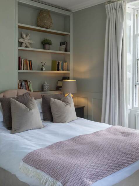 Cozy bedroom with a large bed, plush pillows, soft blanket, bedside lamps, vintage phone, and a window with countryside views