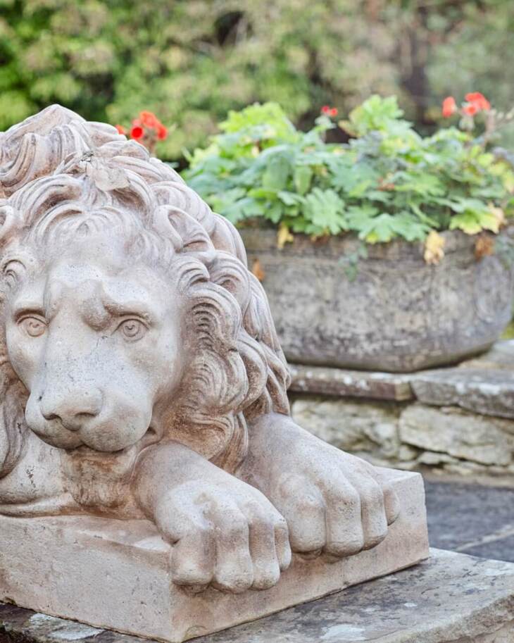 Detailed stone sculpture of a reclining lion in the hotel garden, near a stone planter with green and red flowers