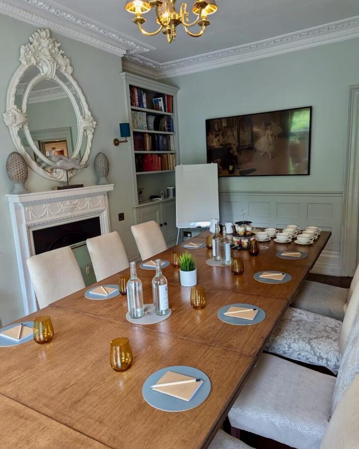 Elegant meeting room with a large wooden table set for a conference, cushioned chairs, decorative mirror, chandelier, and refreshments