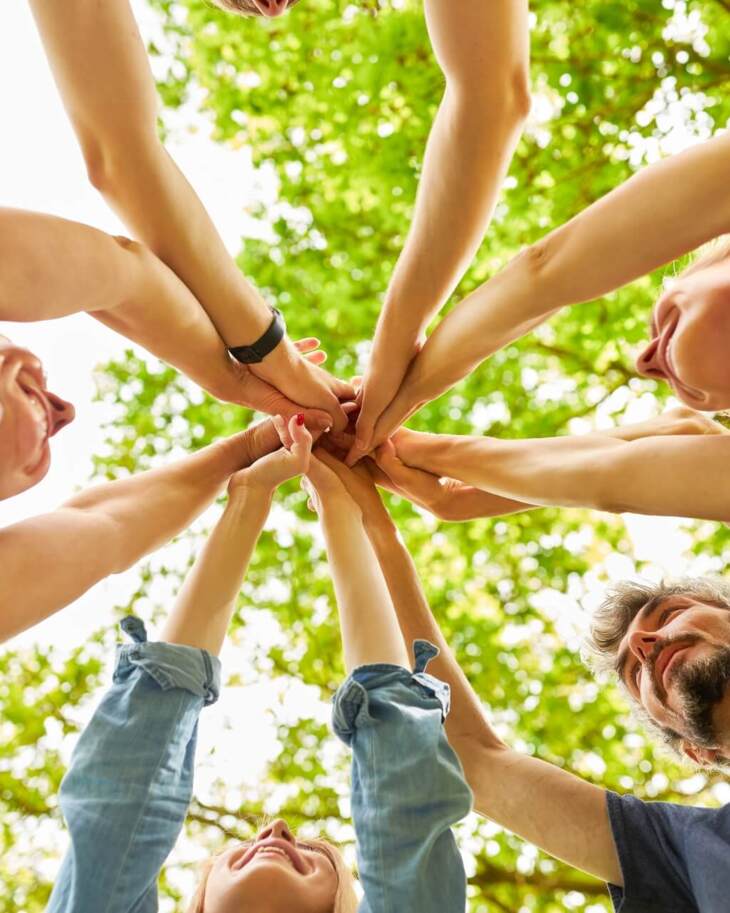 Group of hotel guests joining hands in a circle outdoors under green trees, enjoying a team-building or wellness activity