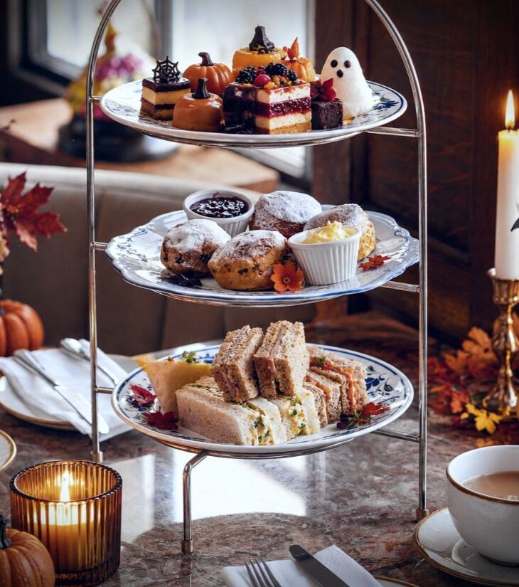 Three-tier afternoon tea with finger sandwiches, scones and Halloween pastries, teacups, mini pumpkins and candles