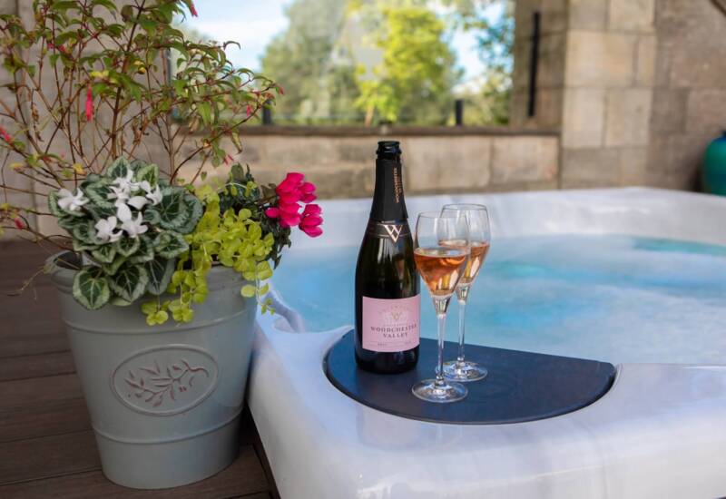 Outdoor hot tub setup with a bottle of Woodchester Valley sparkling wine and two filled glasses beside a large decorative flowerpot