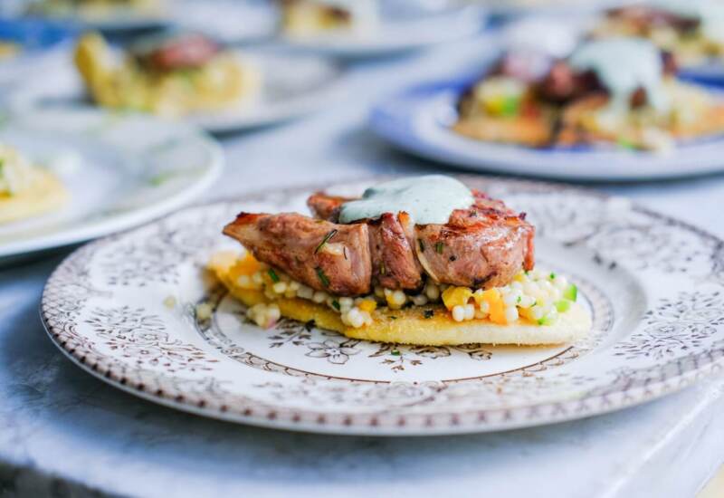 Grilled meat topped with herb sauce served on a bed of pearl couscous and vegetables on a decorative plate