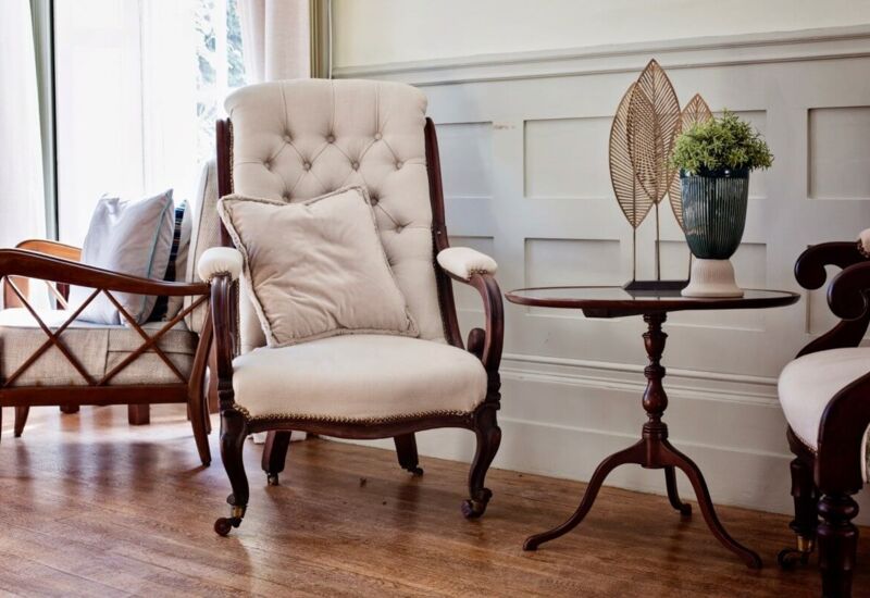 Cozy seating area with vintage tufted armchair, wooden side table with decorative plant, and soft natural light in a classic lounge