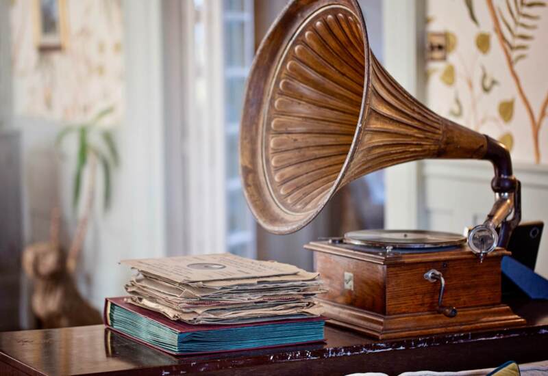 Vintage gramophone with a large brass horn and stacked old vinyl records on a polished wooden table in a cozy hotel lounge.