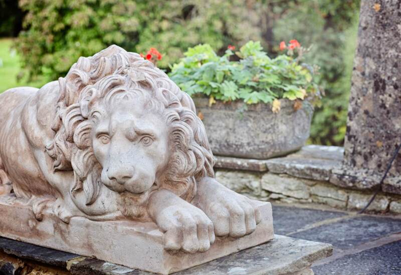 Detailed stone sculpture of a reclining lion in the hotel garden, near a stone planter with green and red flowers