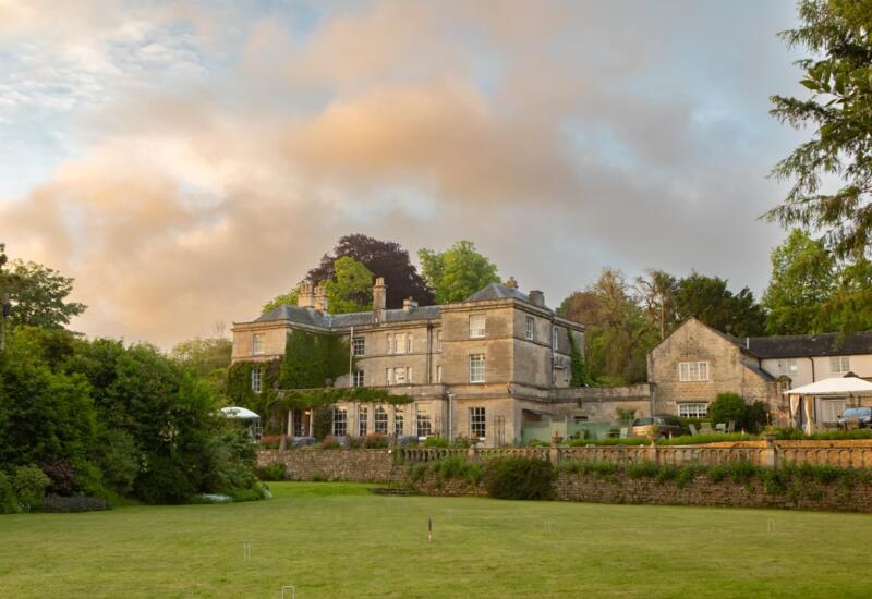 Elegant historic stone manor surrounded by lush greenery with outdoor seating and garden space for relaxation.