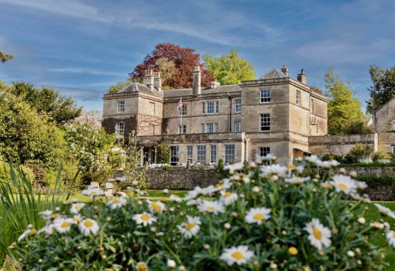 Historic stone country house hotel surrounded by lush gardens and blooming daisies under a clear blue sky