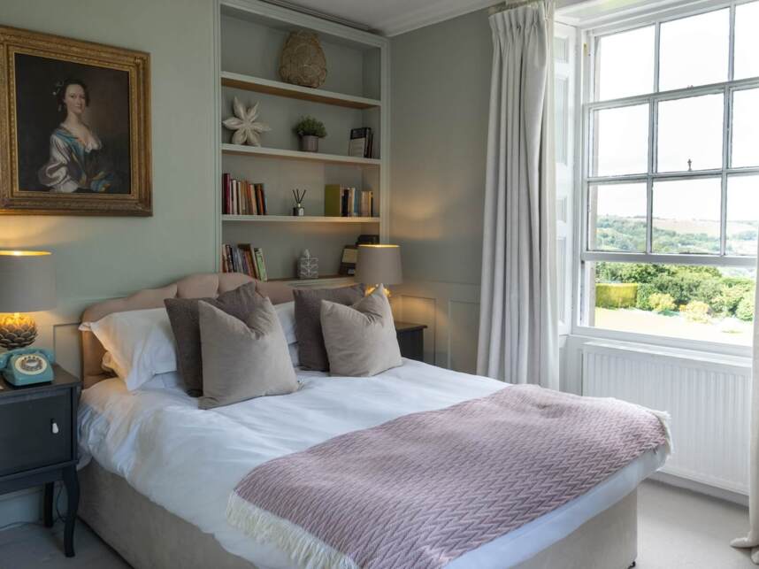 Cozy bedroom with a large bed, plush pillows, soft blanket, bedside lamps, vintage phone, and a window with countryside views