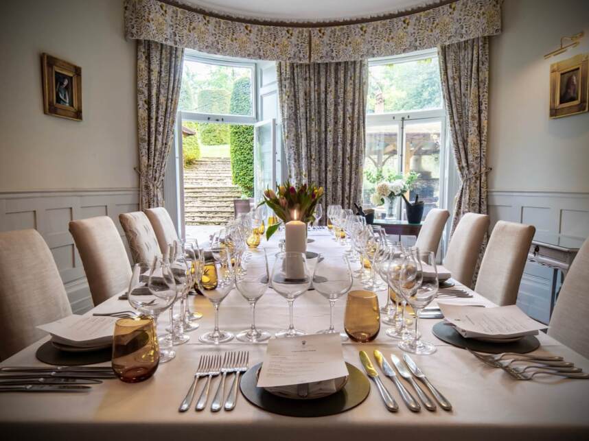 Elegant dining room with a long table set for a formal meal, floral centerpiece, candle, and patterned curtains by garden steps