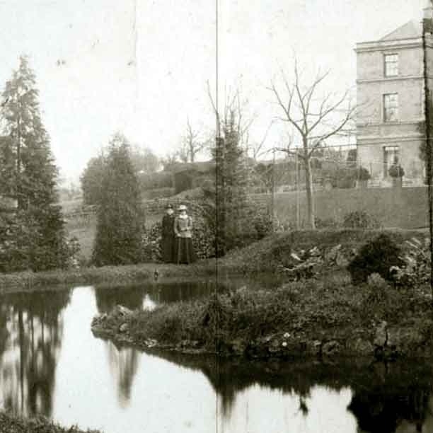 Historic hotel garden with pond, mature trees, and a classic building, showcasing a serene outdoor space for guest relaxation