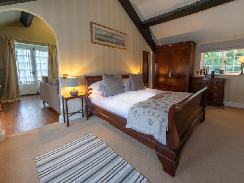 Cozy bedroom with wooden sleigh bed, soft lighting, wooden wardrobe, striped rug, and window with garden view