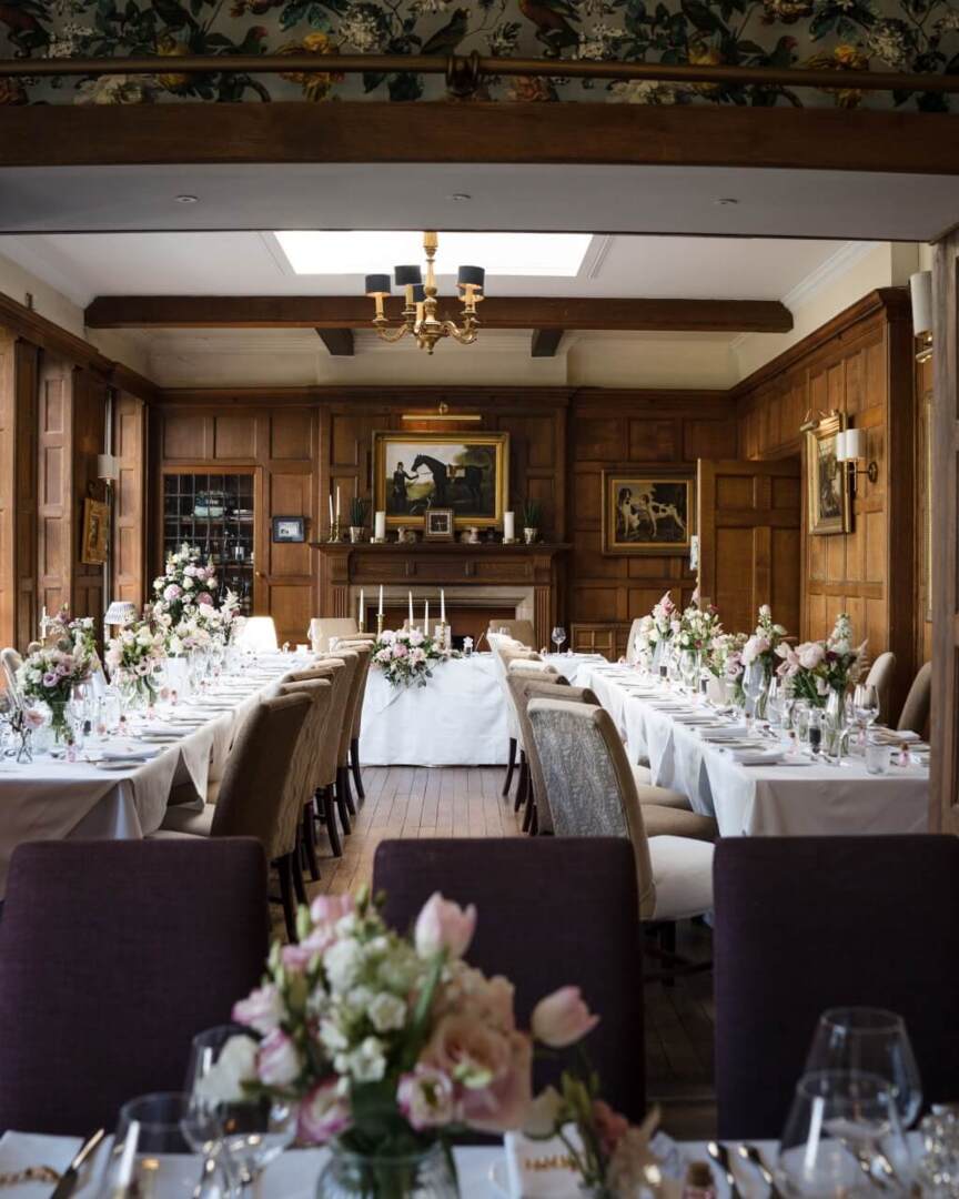 Elegant dining room with wood paneling, floral centerpieces, white table linens, and classic chandelier, set for a formal event