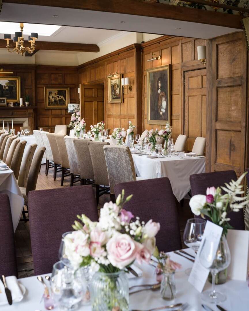Elegant dining room with long tables set for event, floral centerpieces, wooden paneled walls, classic paintings, and soft lighting