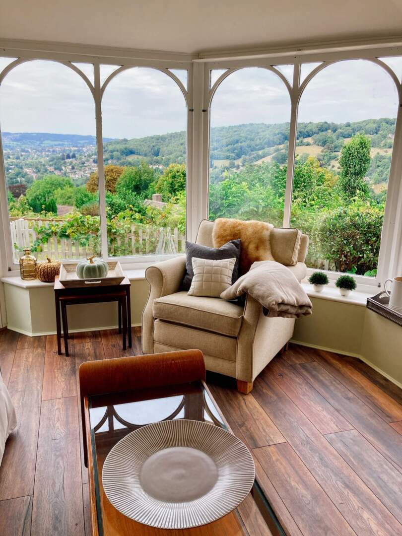 Cozy corner armchair with cushions and throw by large arched windows offering scenic views of green hills and village rooftops