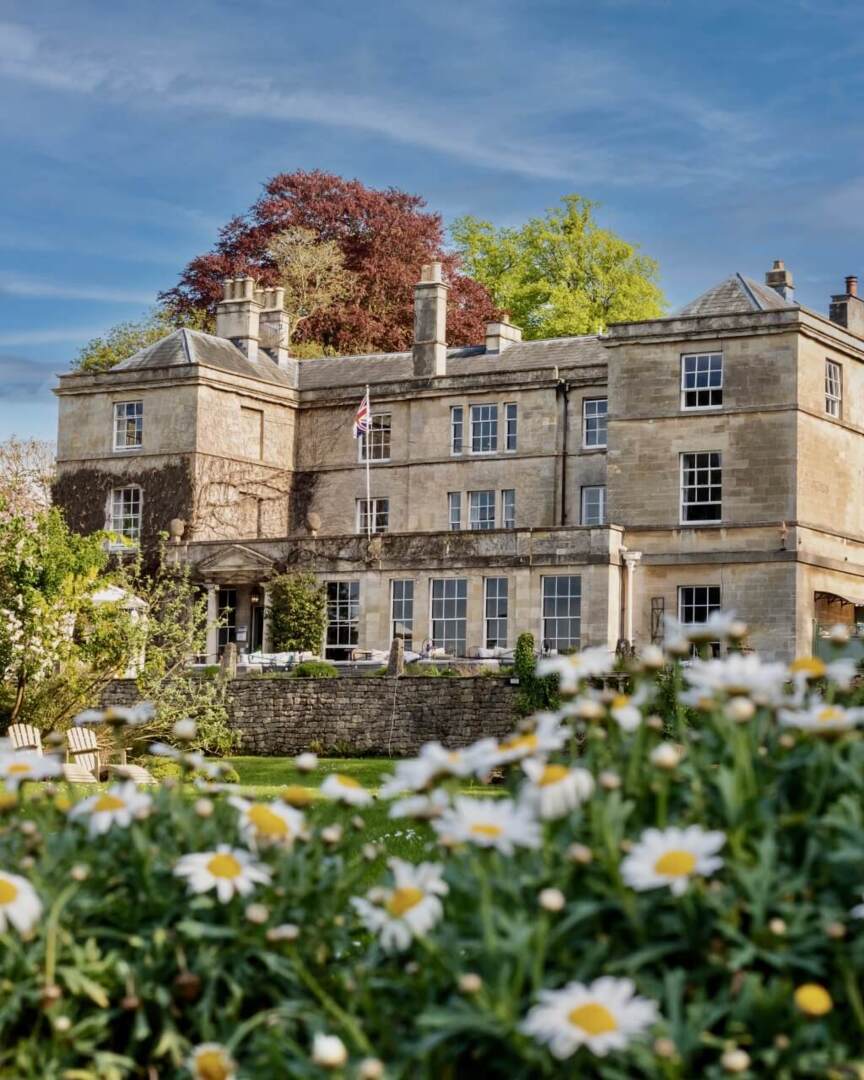 Historic stone country house hotel surrounded by lush gardens and blooming daisies under a clear blue sky