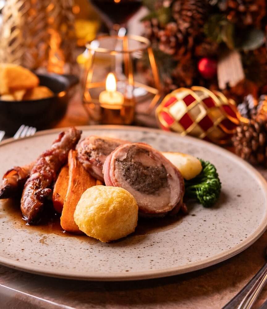 Festive holiday dining plate with roasted meat, vegetables, crispy sides, red wine glass, and warm candlelight ambiance