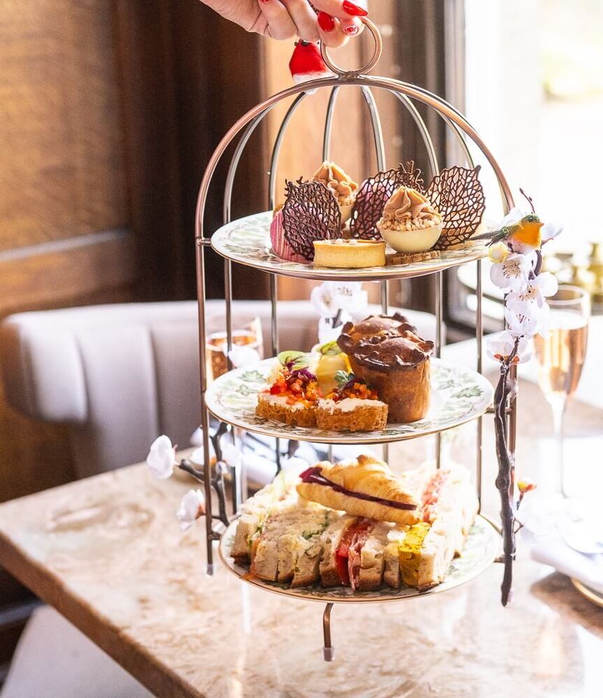 Elegant three-tier afternoon tea stand with assorted sandwiches, pastries, sweets, and a glass of rosé on a marble table