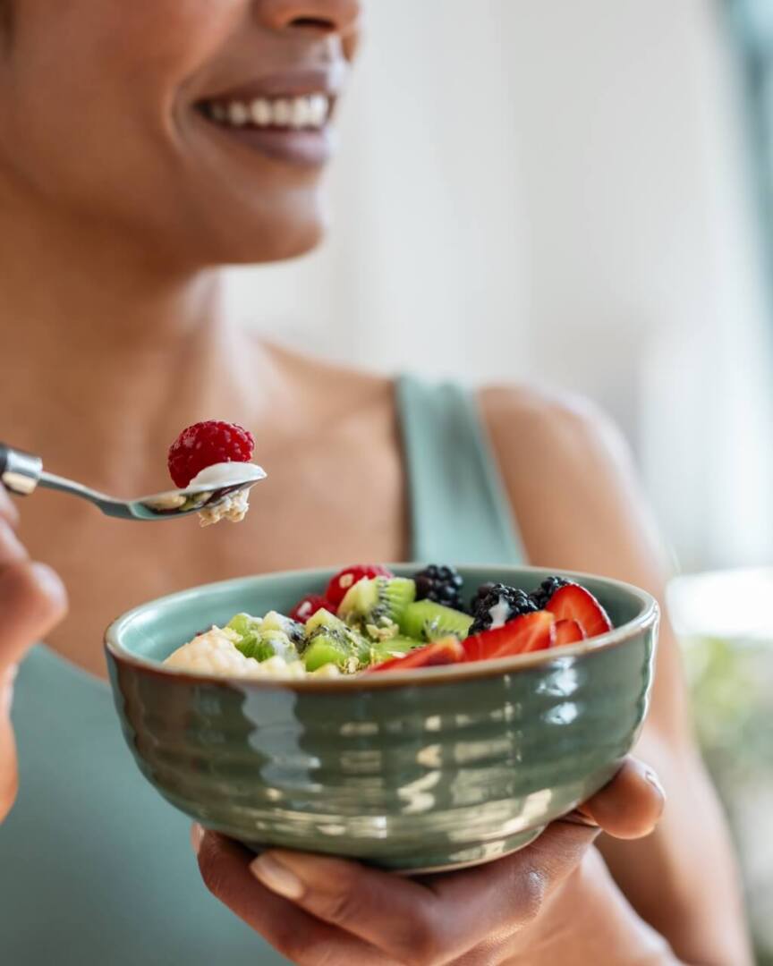 Guest enjoying a fresh fruit bowl with strawberries, kiwi, blackberries, raspberries, and creamy yogurt in a bright, airy breakfast setting