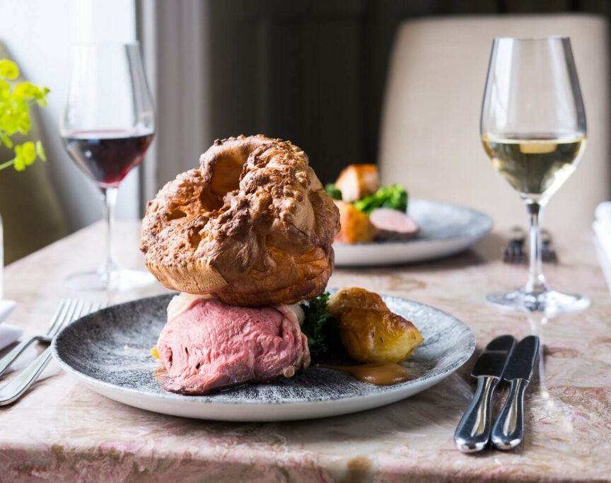 Elegant dining with roasted beef, Yorkshire pudding, side vegetables, paired with glasses of red and white wine on a marble table