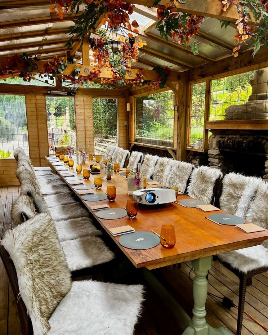 Cozy rustic dining room with wooden table, fur-covered chairs, autumn decor, glassware, and a projector for presentations