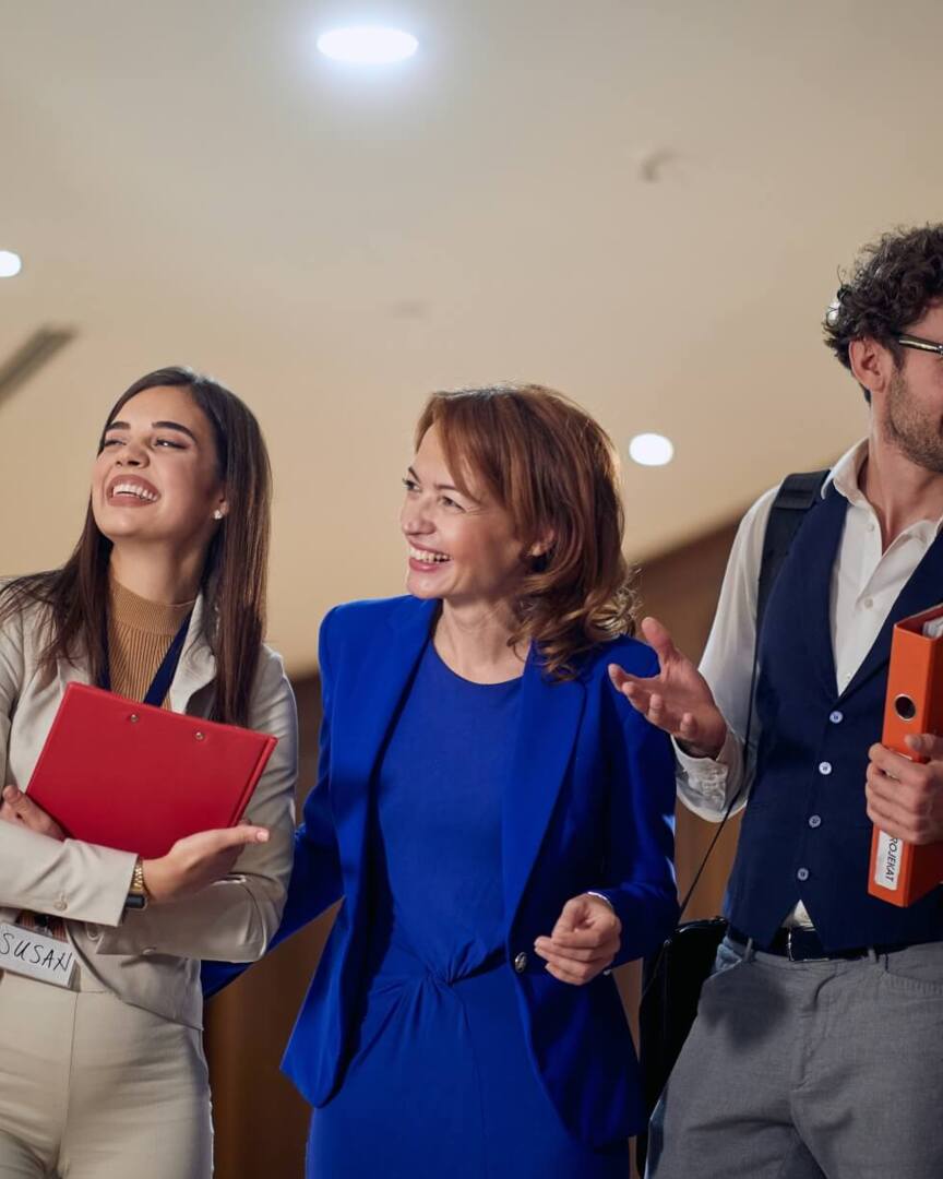 Group of professionally dressed colleagues smiling and chatting in a hotel conference area with wood panel walls and bright lighting
